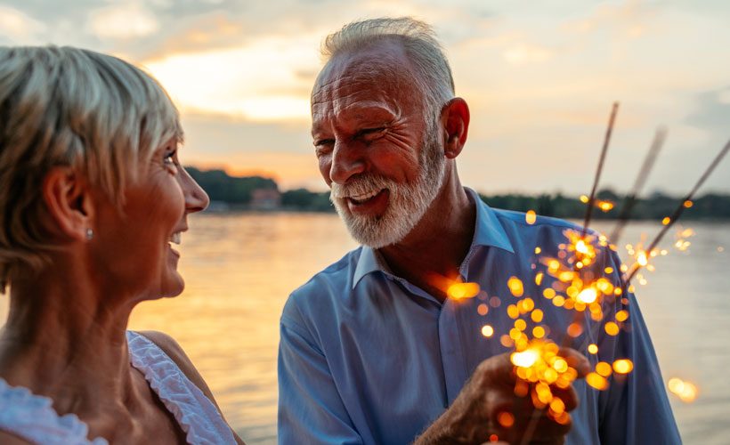 Ein älteres Paar feiert am Ufer eines Sees mit Sternspritzern in der Hand.